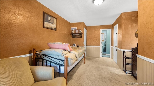 bedroom featuring carpet floors, a textured wall, and a wainscoted wall