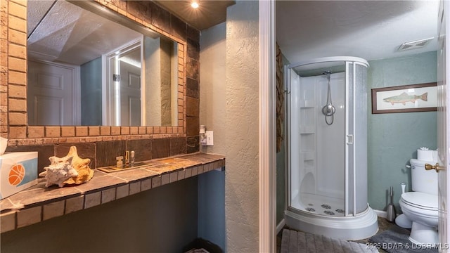 full bathroom with vanity, visible vents, toilet, a stall shower, and a textured wall