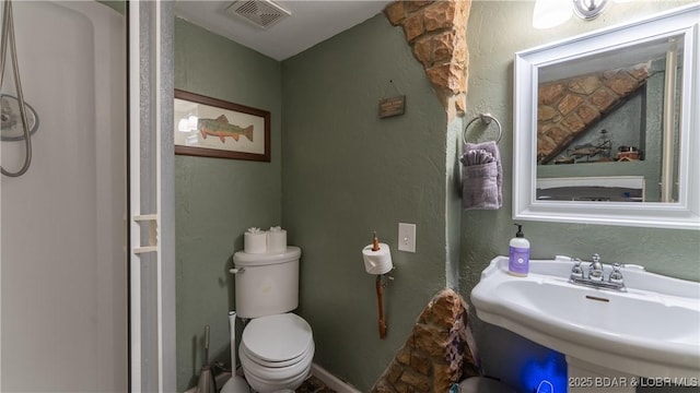 bathroom with toilet, a textured wall, a sink, and visible vents