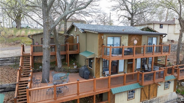 back of property with a shingled roof, a wooden deck, a balcony, and stairs