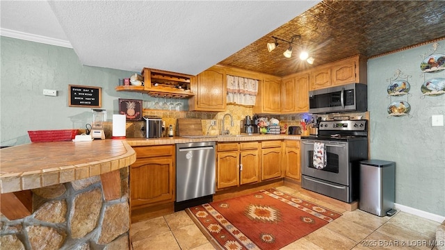 kitchen with appliances with stainless steel finishes, a textured wall, light tile patterned floors, decorative backsplash, and a sink
