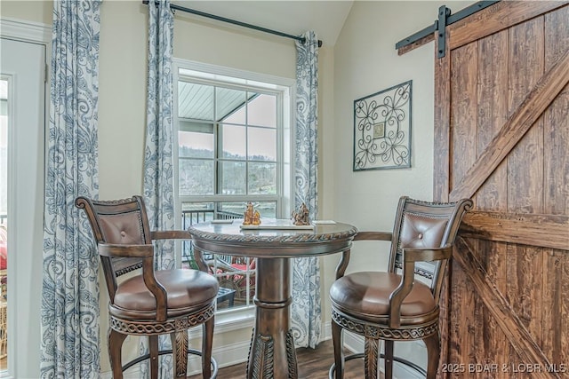 dining area with a barn door, wood finished floors, vaulted ceiling, and baseboards