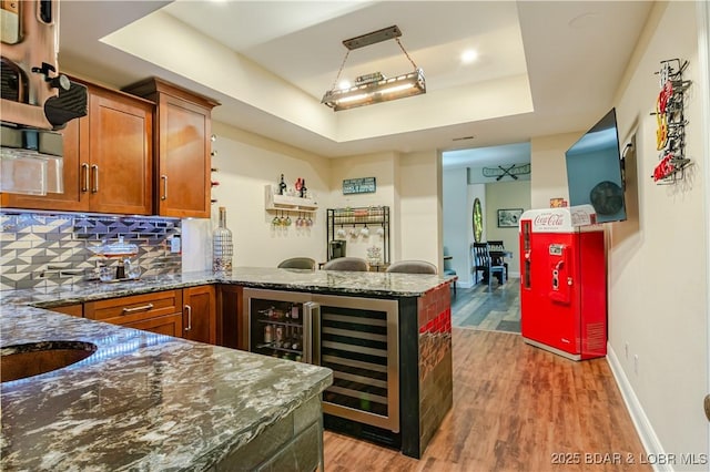 kitchen with brown cabinetry, a peninsula, light wood-style flooring, a raised ceiling, and dark stone counters