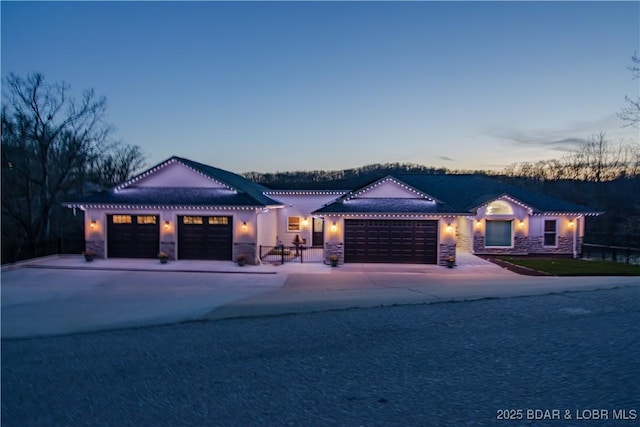 view of front of property featuring stone siding, driveway, a garage, and fence
