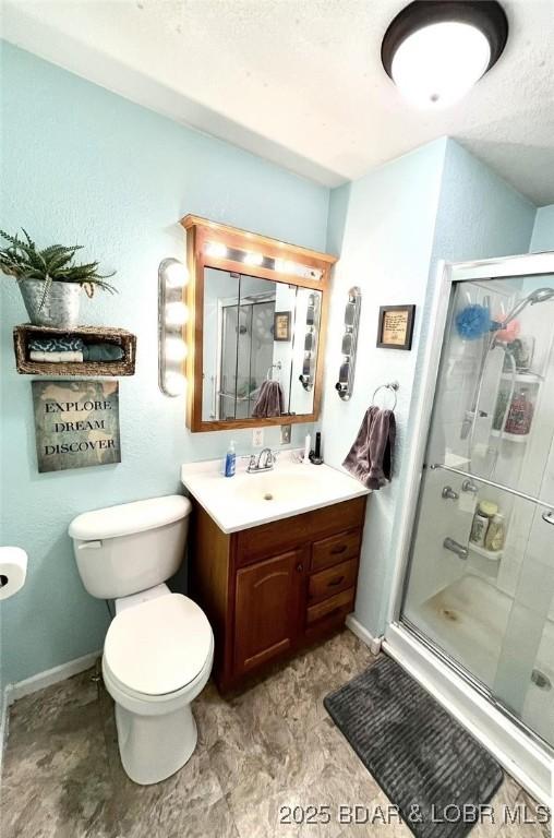 full bathroom with toilet, a stall shower, baseboards, and vanity