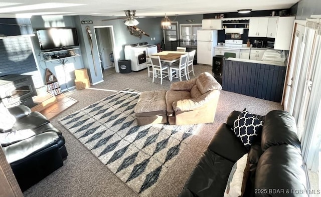 living area featuring baseboards, carpet floors, a wood stove, independent washer and dryer, and ceiling fan