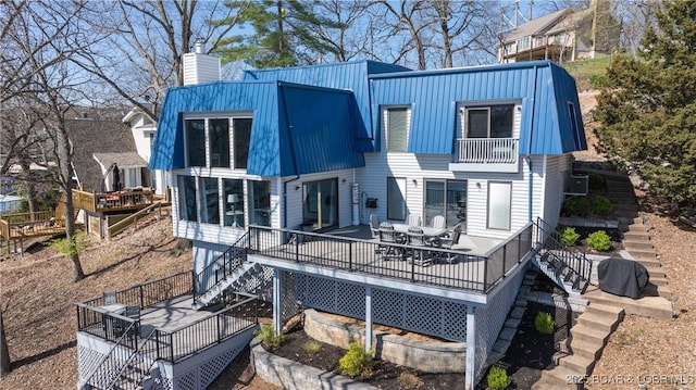 back of house with stairs, a wooden deck, a chimney, a balcony, and metal roof