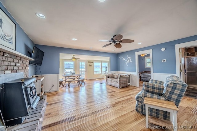 33724 Ivy Bnd, Stover, MO 65078 - living room featuring a wainscoted wall, a ceiling fan, a wood stove, recessed lighting, and light wood-style floors