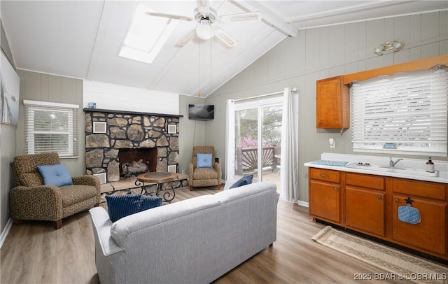29829 Sheldy Dr, Rocky Mount, MO 65072 - living area with ceiling fan, a stone fireplace, wood walls, light wood finished floors, and lofted ceiling with skylight