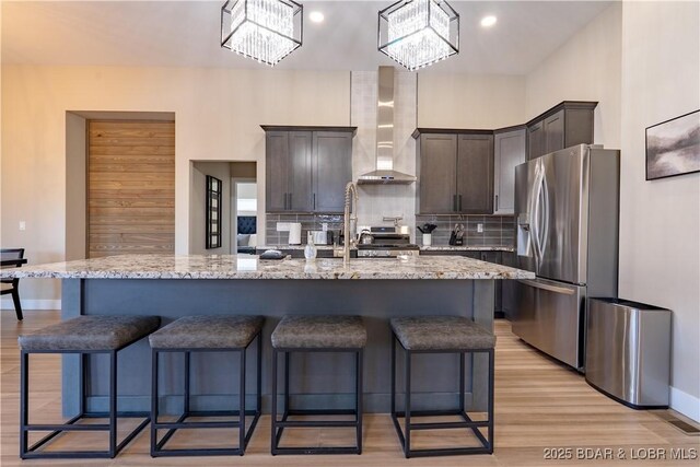613 Cove Cir, Sunrise Beach, MO 65079 - kitchen featuring stainless steel refrigerator with ice dispenser, wall chimney exhaust hood, dark brown cabinetry, decorative backsplash, and light wood finished floors