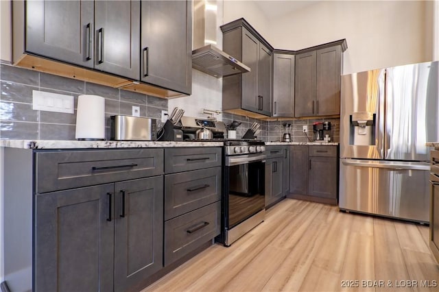 613 Cove Cir, Sunrise Beach, MO 65079 - kitchen with stainless steel appliances, wall chimney exhaust hood, light stone counters, backsplash, and light wood finished floors