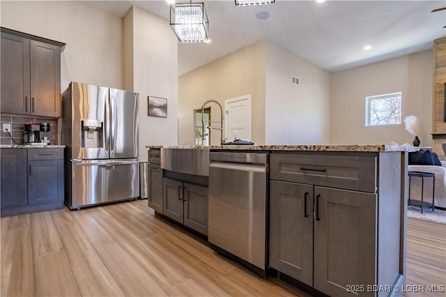 613 Cove Cir, Sunrise Beach, MO 65079 - kitchen featuring stainless steel appliances, light wood-style floors, light stone counters, a kitchen island with sink, and a sink
