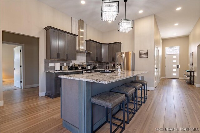 613 Cove Cir, Sunrise Beach, MO 65079 - kitchen featuring stainless steel refrigerator with ice dispenser, wall chimney range hood, dark brown cabinetry, a kitchen breakfast bar, and tasteful backsplash