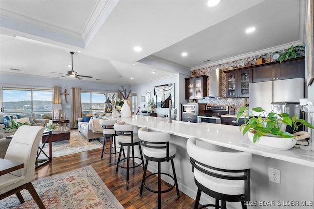 248 Palisades Condo Dr Unit 4A, Lake Ozark, MO 65049 - kitchen with stainless steel appliances, ornamental molding, wall chimney exhaust hood, dark brown cabinets, and a breakfast bar area