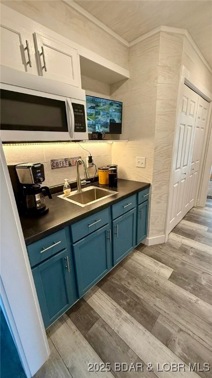 bar with a sink, backsplash, white microwave, and dark wood-type flooring