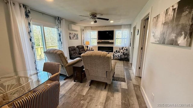 living room with a wall mounted AC, ceiling fan, wood finished floors, and a wealth of natural light