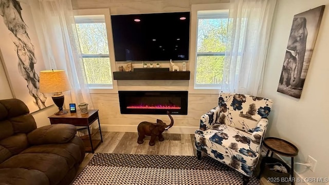 sitting room featuring baseboards, a glass covered fireplace, wood finished floors, and a healthy amount of sunlight