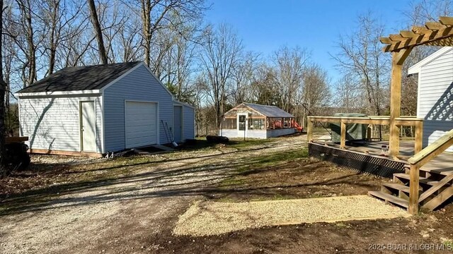 view of yard with dirt driveway, a wooden deck, an outbuilding, and a detached garage