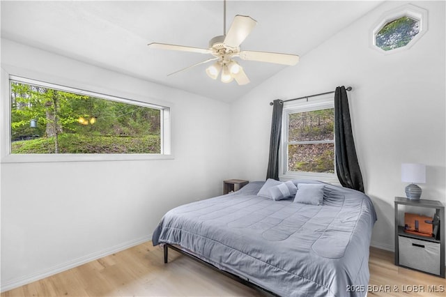 bedroom with wood finished floors, baseboards, multiple windows, and vaulted ceiling