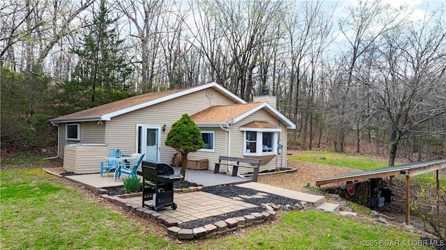 rear view of property featuring a patio, a chimney, a shingled roof, and a lawn