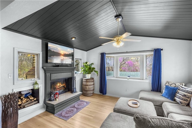 living room with a glass covered fireplace, a wealth of natural light, vaulted ceiling, and wood finished floors