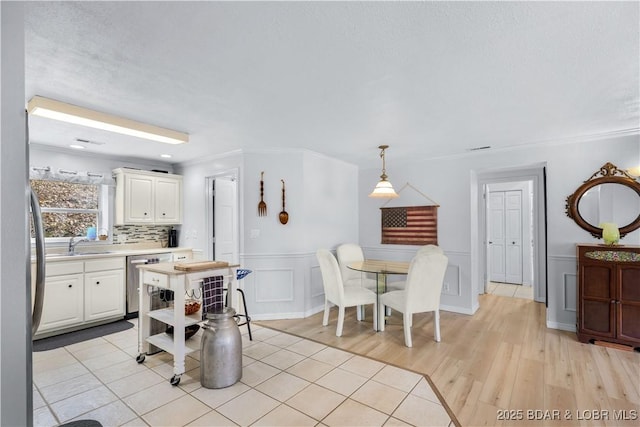dining area featuring a decorative wall, light wood-style floors, ornamental molding, and a wainscoted wall