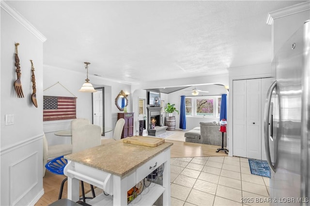 kitchen featuring ceiling fan, a lit fireplace, stainless steel refrigerator, open shelves, and ornamental molding