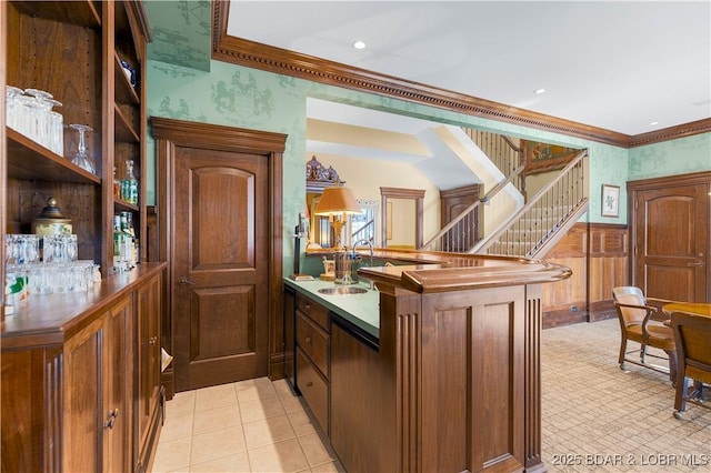 kitchen featuring ornamental molding, a peninsula, a sink, wallpapered walls, and wainscoting