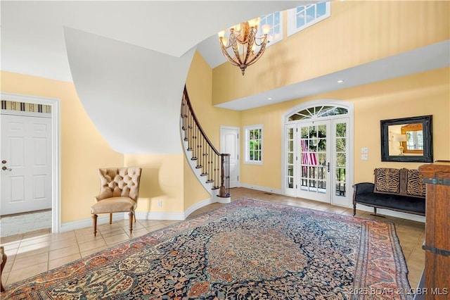 foyer entrance featuring tile patterned floors, a chandelier, stairs, baseboards, and a towering ceiling