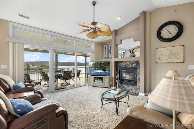 living area with a glass covered fireplace, vaulted ceiling, a ceiling fan, visible vents, and plenty of natural light