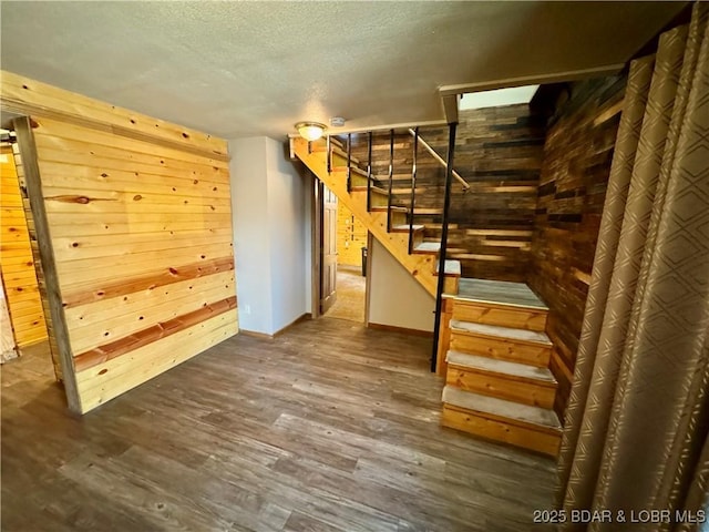 below grade area with stairway, dark wood-style floors, wooden walls, baseboards, and a textured ceiling