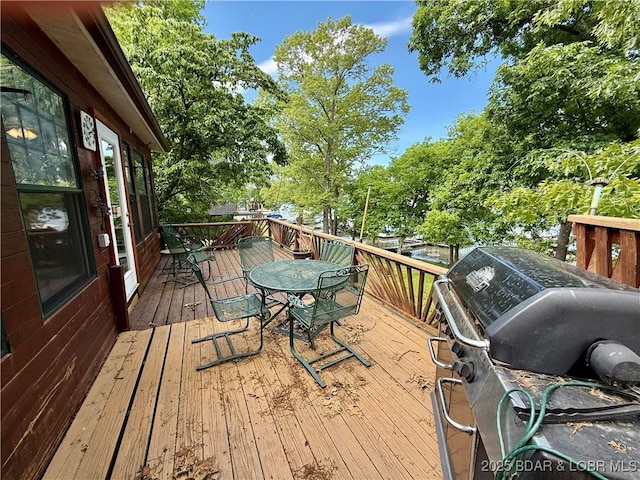 wooden deck featuring outdoor dining area, area for grilling, and view of scattered trees