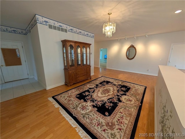 foyer entrance featuring track lighting, light wood finished floors, baseboards, and a notable chandelier