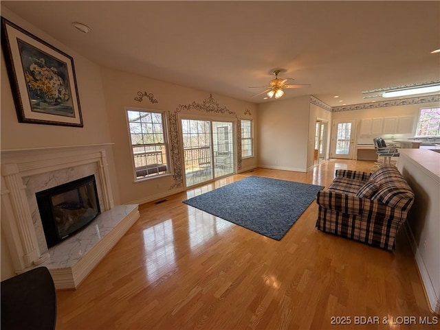 living area with baseboards, ceiling fan, light wood-style flooring, and a fireplace
