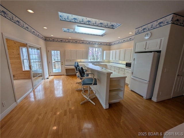 kitchen with light countertops, a center island, white cabinets, and freestanding refrigerator