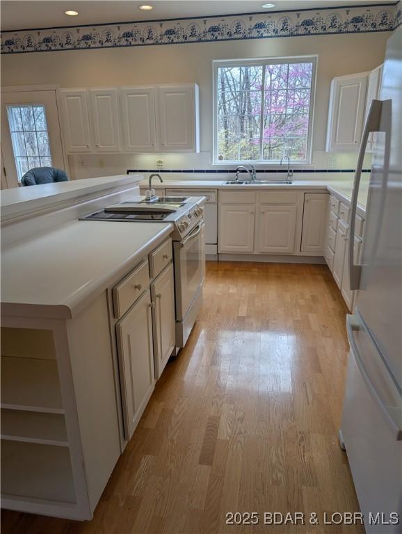 kitchen featuring light wood-type flooring, white cabinetry, a wealth of natural light, and white appliances