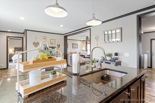 kitchen with a sink, crown molding, washer and clothes dryer, decorative light fixtures, and dark stone countertops