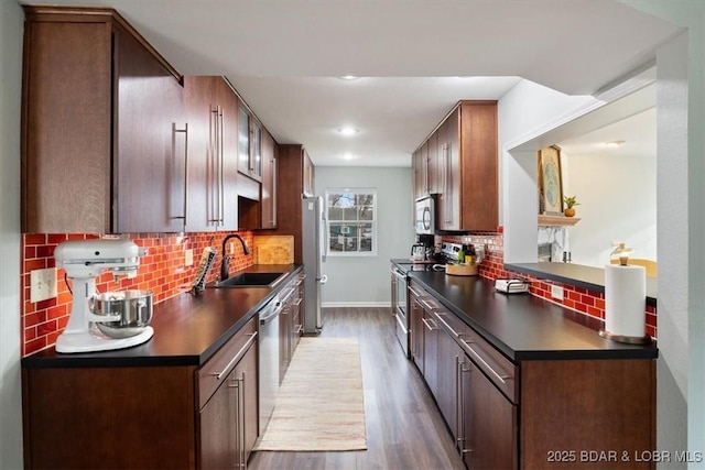 kitchen with stainless steel appliances, backsplash, dark countertops, wood finished floors, and a sink