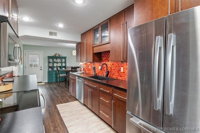 kitchen with stainless steel appliances, dark countertops, visible vents, a sink, and tasteful backsplash