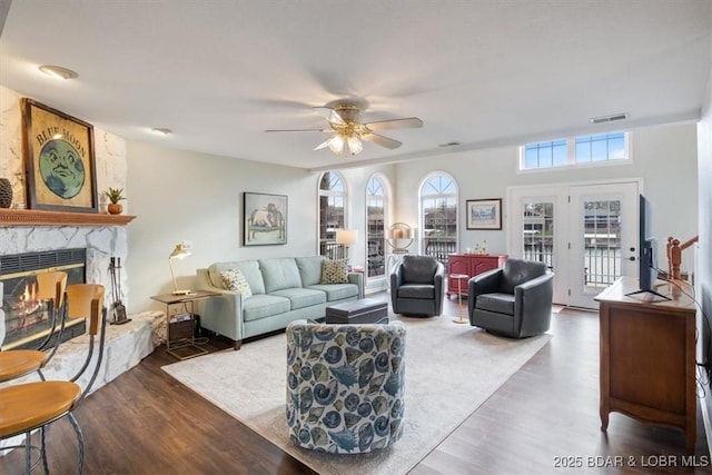 living room with a high end fireplace, wood finished floors, visible vents, and a ceiling fan