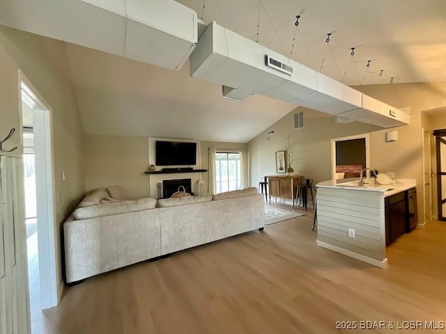 living room with a fireplace, light wood-style floors, visible vents, and vaulted ceiling