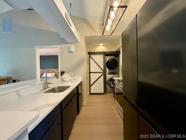 kitchen featuring light wood-type flooring, black appliances, light countertops, a sink, and stacked washer / drying machine