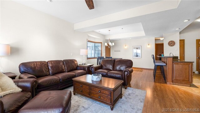 living room featuring baseboards, a raised ceiling, a notable chandelier, light wood-style floors, and recessed lighting