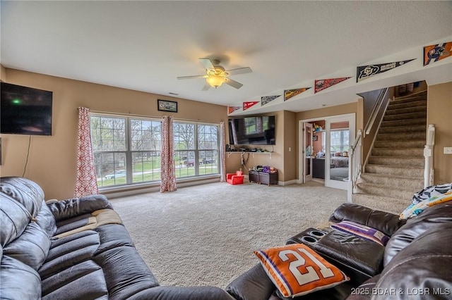 carpeted living area with ceiling fan and stairway