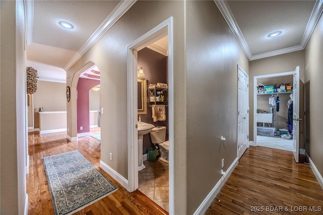 hallway featuring crown molding, arched walkways, and wood finished floors