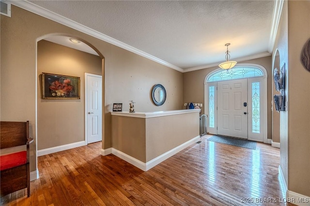 foyer entrance with ornamental molding, wood-type flooring, baseboards, and arched walkways