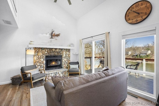 living area featuring wood finished floors, baseboards, a stone fireplace, and visible vents