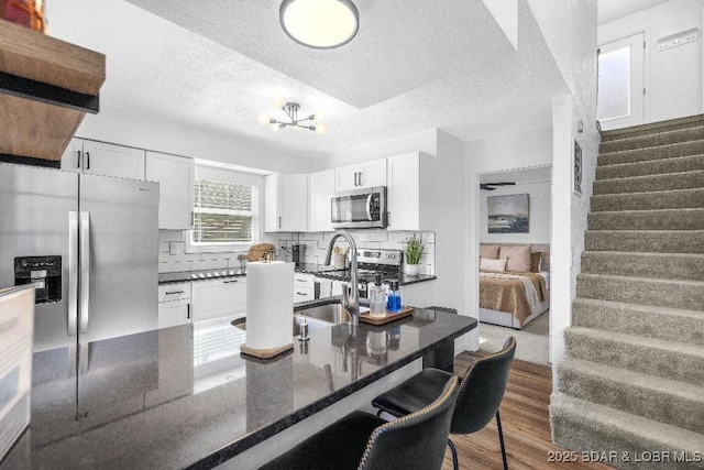 kitchen with a sink, a textured ceiling, white cabinetry, wood finished floors, and stainless steel appliances