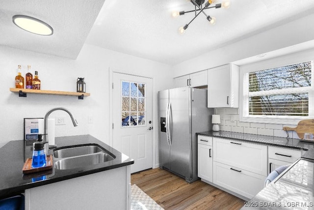 kitchen with stainless steel fridge, a sink, a textured ceiling, white cabinetry, and wood finished floors