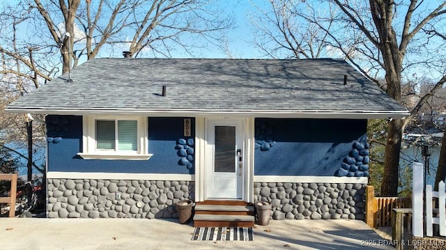view of front facade with roof with shingles, entry steps, fence, and stucco siding